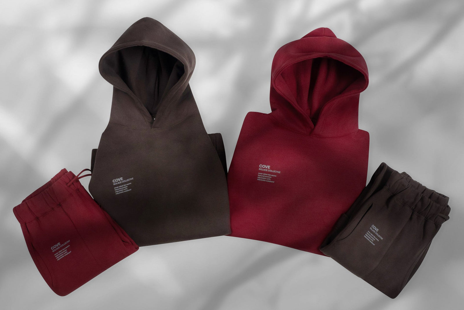 Brown and deep-red SOLACE Collective hoodies and matching pants arranged on a light surface.